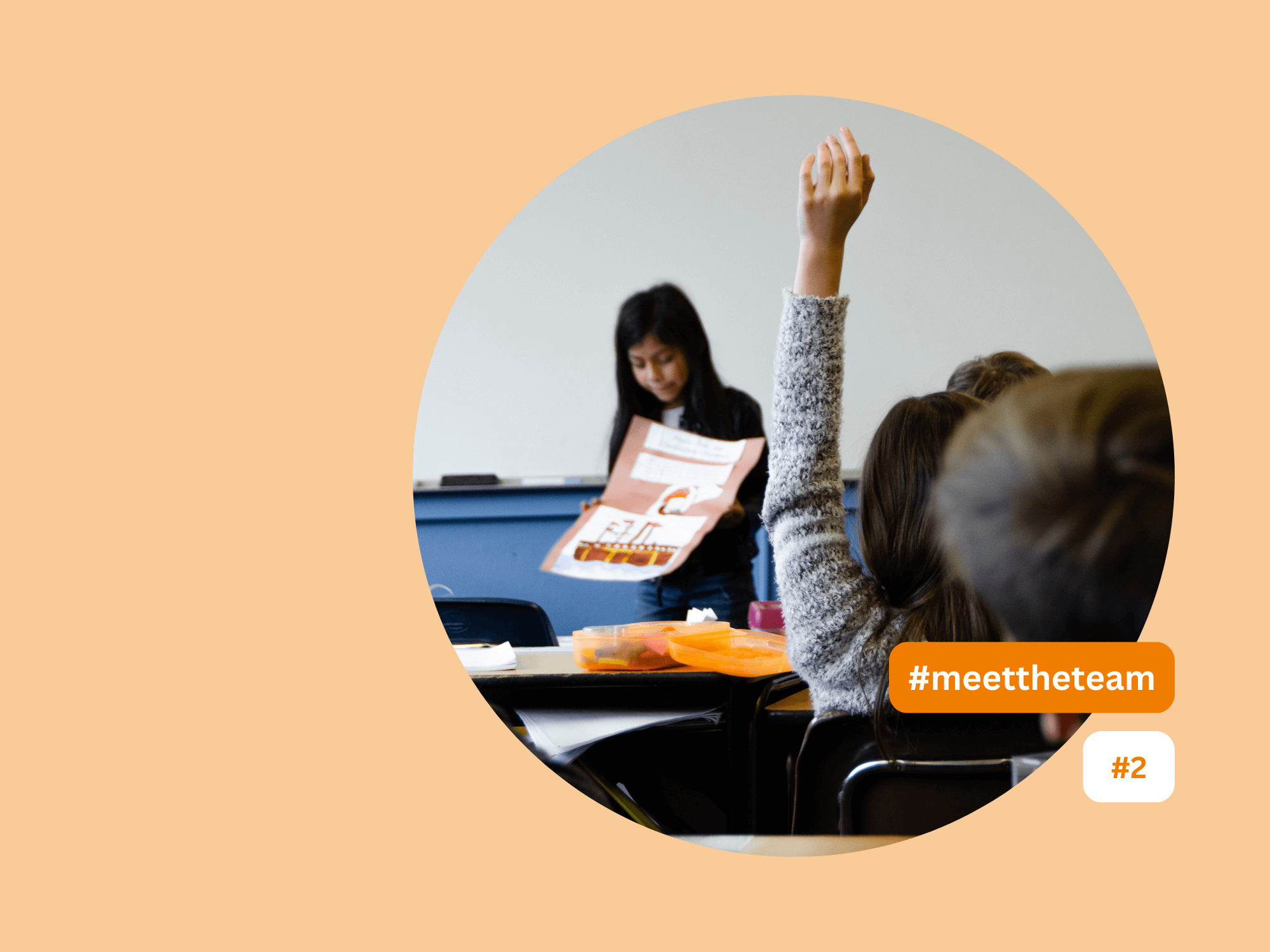 The image shows a classroom. A young girl is holding a poster and presenting in the front of the classroom. A boy is holding is hand up.