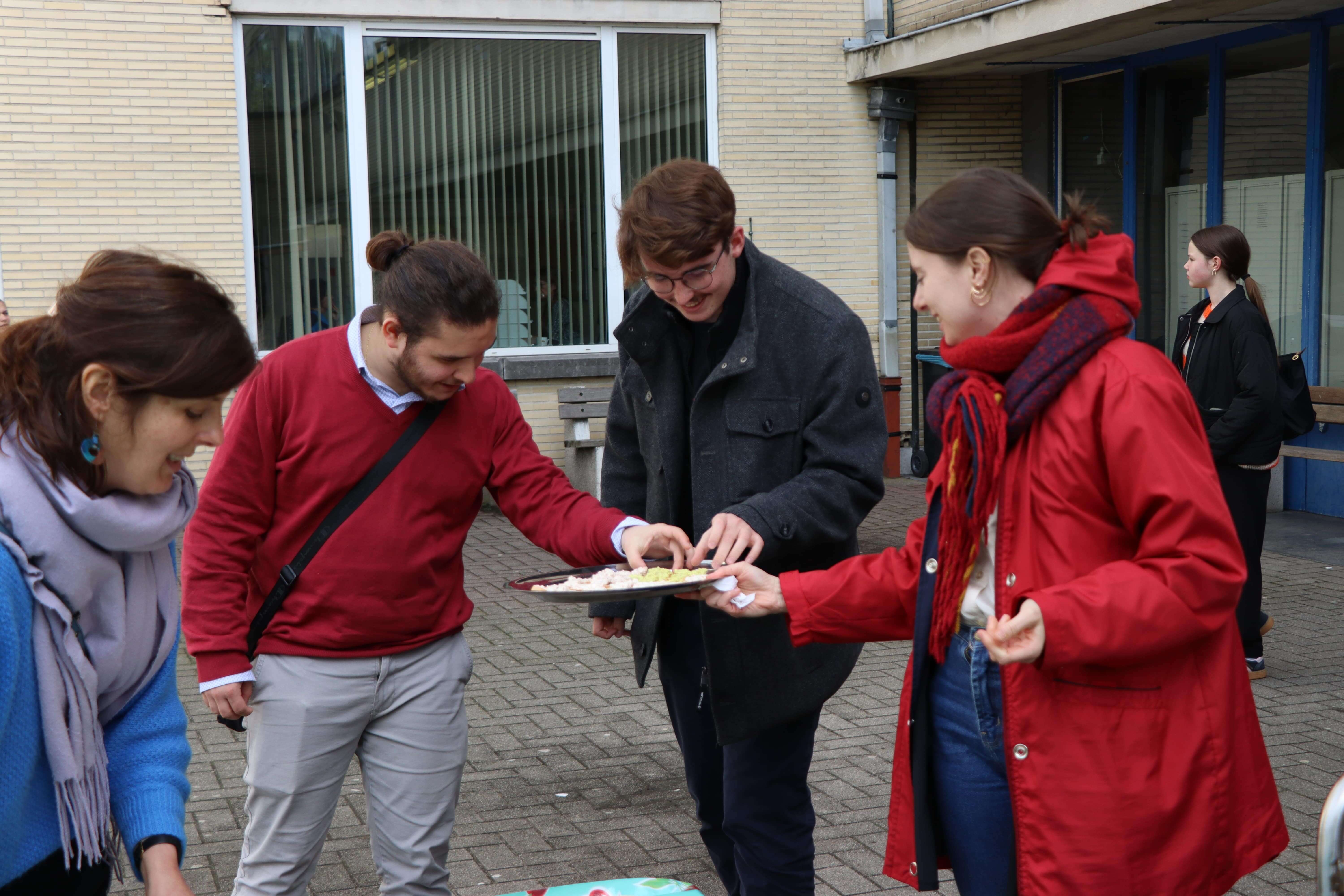 Two people handing out food samples to two male students